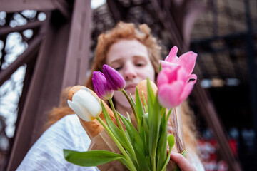 a girl in a white shirt and with red hair holds a bouquet of colorful tulips