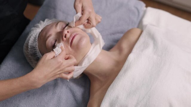 wipes off, nourishing mask, Face cleaning. Beautician wipes off remaining mask from the client's face with a napkin, in a cosmetology clinic