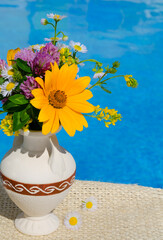 A bouquet of wild flowers in a small vase against the background of the pool.