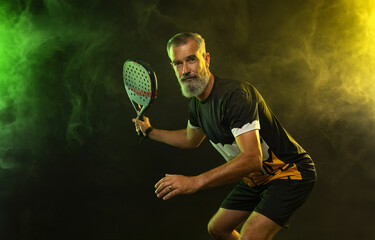 The old man. Padel tennis player with racket. Man athlete with paddle racket on court with neon colors. Sport concept. Download a high quality photo for the design of a sports app or betting site.