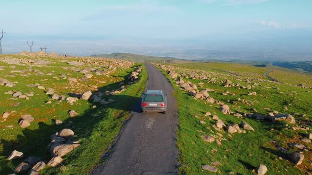 tourists by car climbed high into mountains of Armenia, view from drone. Mount Aragats, drone follows moving car in mountains high. Beautiful landscape from bird's eye view.