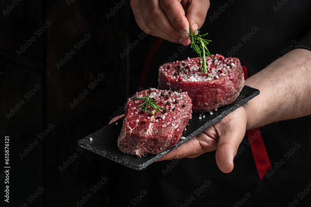 Wall mural preparing fresh beef or pork on a dark background. chef salts steak in a freeze motion with rosemary