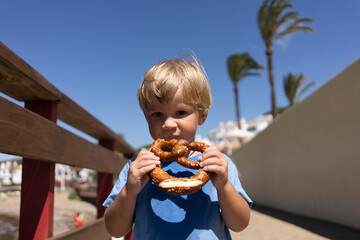 little boy blond blue t-shirts eats pretzel on a summer day