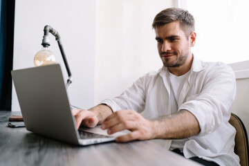 Cheerful man shopping online on laptop while sitting at table