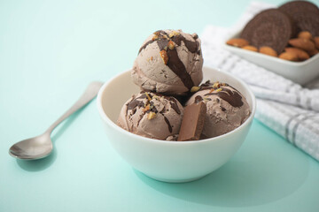 Chocolate ice cream decorated with nuts and chocolate icing, in a white bowl, blue background. Summer homemade cooling desserts