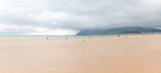 Fototapeta na wymiar People walking on a wide beach on a cloudy morning, Laredo, Cantabria, Spain 
