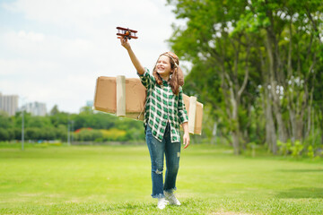 Obraz premium Portrait of red hair kid in pilot costume holding wooden plane running in summer field