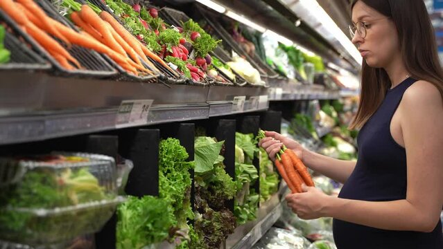 Young Pregnant Caucasian woman buying organic food at grocery store. Expecting female choosing healthy food. Healthy pregnancy, maternity and lifestyle.