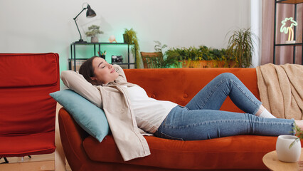 Portrait of tired young woman enjoy relaxing on home sofa in room. Happy pretty girl lying on couch resting napping after hard working day, closed her eyes, put hands behind head, stress free, rest