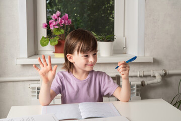 Girl sits at the table and holds a pen in her left hand. Left handed child. International Left Handers Awareness Day