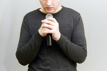 A young man holds a microphone with both hands and speaks with restraint. Public speaking, lyrical...