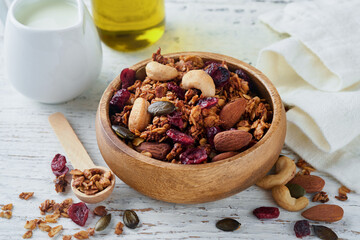 Homemade granola in glass jar with greek yogurt or milk and cashews, almonds, pumpkin with dried cranberry seeds in on white rustic wooden table background. Healthy energy breakfast or snack. Top view