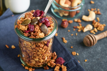 Homemade granola in glass jar with greek yogurt or milk and cashews, almonds, pumpkin with dried cranberry seeds in dark grey table background. Healthy energy breakfast or snack. Top view