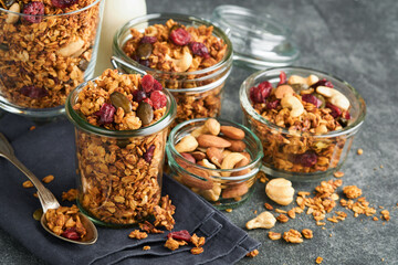 Homemade granola in glass jar with greek yogurt or milk and cashews, almonds, pumpkin with dried cranberry seeds in dark grey table background. Healthy energy breakfast or snack. Top view