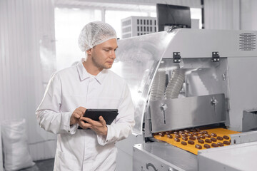 Worker control quality of sweets candy with computer tablet. Concept modern chocolate factory...