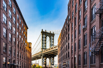 famous Manhattan Bridge with Empire State in the arch seen from a narrow alley enclosed by two...