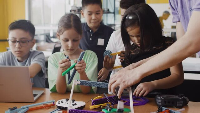 Young teacher learning children around the table in a class at a robotics lesson how to assemble a moving robot by hand. Concept of technological modern education