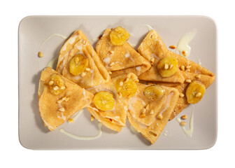 Crepes on gray rectangular plate isolated on white. Thin pancakes served with bananas, pine nuts and sweet sauce.