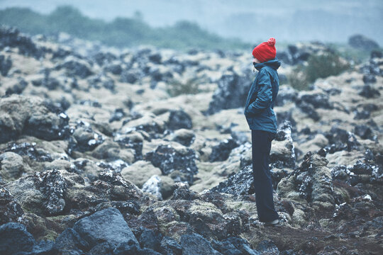 Woman in waterproof clothing walks on volcanic Lava fields on background of mountains of Iceland.
