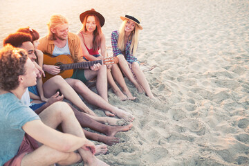 Happy group of friend having party and playing guitar on the beach