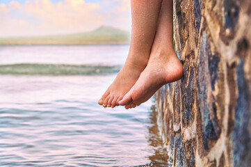 Young girl's wet bare feet dangling from the stone jetty
