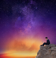Fototapeta premium Businessman works on laptop with internet connection over a mountain with a sky full of stars