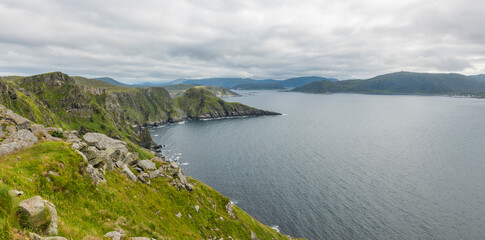 Amazing view from island Runde on the ocean and surrounding mountains. Summertime on Runde island, Her&oslash;y, M&oslash;re og Romsdal. cloudy day during summer. Grass and rocks in the foreground.
