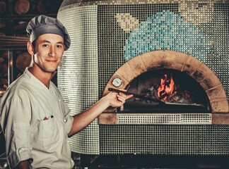 Food concept. Preparing traditional italian pizza. Young smiley chef in white uniform holds in his...