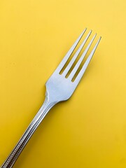 Stainless steel silver fork, isolated, resting on mustard - yellow background at an angle. Imperfections and slight shadows visible.