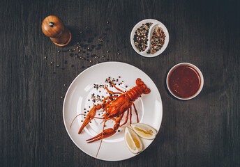Food concept. Boiled big red fresh crawfish in white plate with lemon slices. Composition with sauce, herbs and pepper grains around. Gray wooden background. Instagram vintage toning effect. Top view.