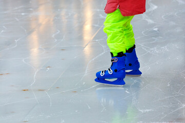 The child learns to skate and stands uncertainly on the ice.