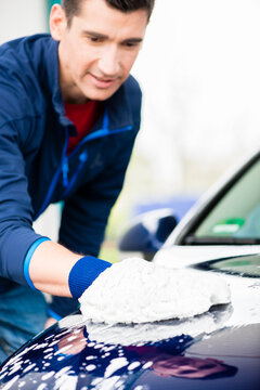Hard-working young man polishing car with white microfiber mitt at auto wash