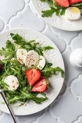 Salad with mozzarella with strawberries, mozzarella and arugula. Healthy light summer salad modern styling on white tile background close up top view