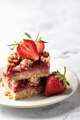 Two pieces of Strawberry granola bars on a pate on white marble background close up. Delisious homemade oat squares for breakfast with copy space