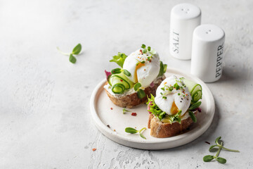 Fototapeta Poached egg sandwich with cucumber and microgreens. Healty breakfast bruschetta on light background. Keto diet, text space obraz
