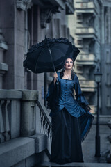 Woman dressed in blue victorian dress stand near old building