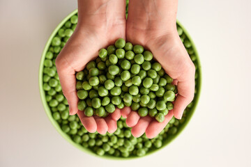 Close-up of a lot of ripe peas in hands, heart shaped. Green pea in a green bowl. Tasty and healthy food. Vegetables