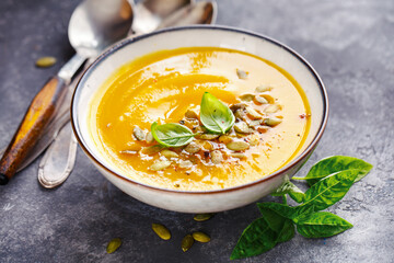Homemade pumpkin soup with basil leaf and pumpkin seeds.