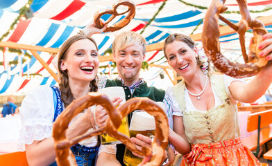 Three friends in beer tent at Dult or Oktoberfest holding giant pretzels up in the air