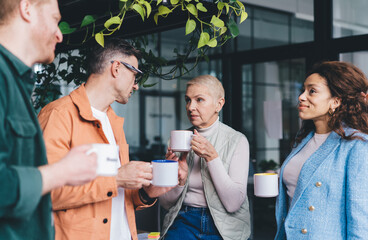 Successful male and female colleagues discussing exchange marketing and business collaboration in office interior, diverse employees with coffee cups analyzing brainstorming teamwork and briefing