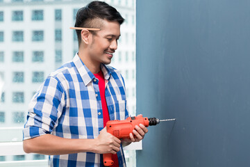 Asian do-it-yourself handyman drilling at wall in skyscraper building