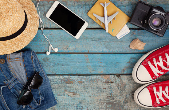 Still life of various items for recreation, clothing, hat, sneakers, camera, passport, telephone, sunglasses, tickets, headset on a wooden blue background. Concept of youth travel, light, economy.