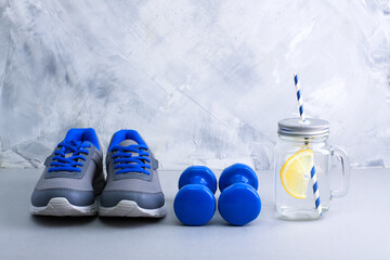 Sport composition with gray sneakers with blue shoelaces, blue dumbbells, mason jar with water...