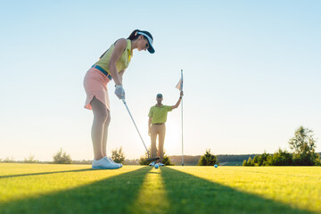 Low-angle side view of an attractive fit woman exercising hitting technique during golf class with...