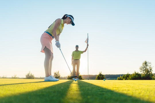 Low-angle side view of an attractive fit woman exercising hitting technique during golf class with an experienced professional player in summer