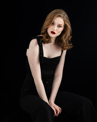 Beauty theme portrait of a beautiful young girl model with freckles on her face in a black dress and black pantyhose on a dark background in the studio