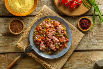 Israeli couscous with sumac and pieces of stewed chicken on a table on a linen napkin in a plate next to spices and vegetables