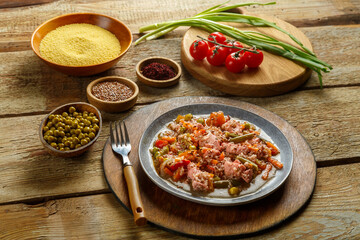 Israeli spice couscous with sumac and chicken pieces on a round wooden stand next to couscous, sumac and vegetables.