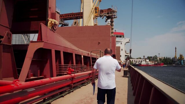 2021-06-09 Mariupol, Ukraine. Ukrtransagro LLC. Shipping agent walks down bulker ship and inspects loading at sea port. Expeditor goes on cargo vessel in face mask. Global trading, transport concept.