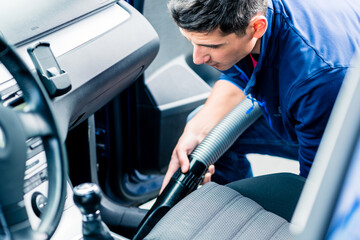 Young hard-working man using vacuum for cleaning the interior of a car at auto wash